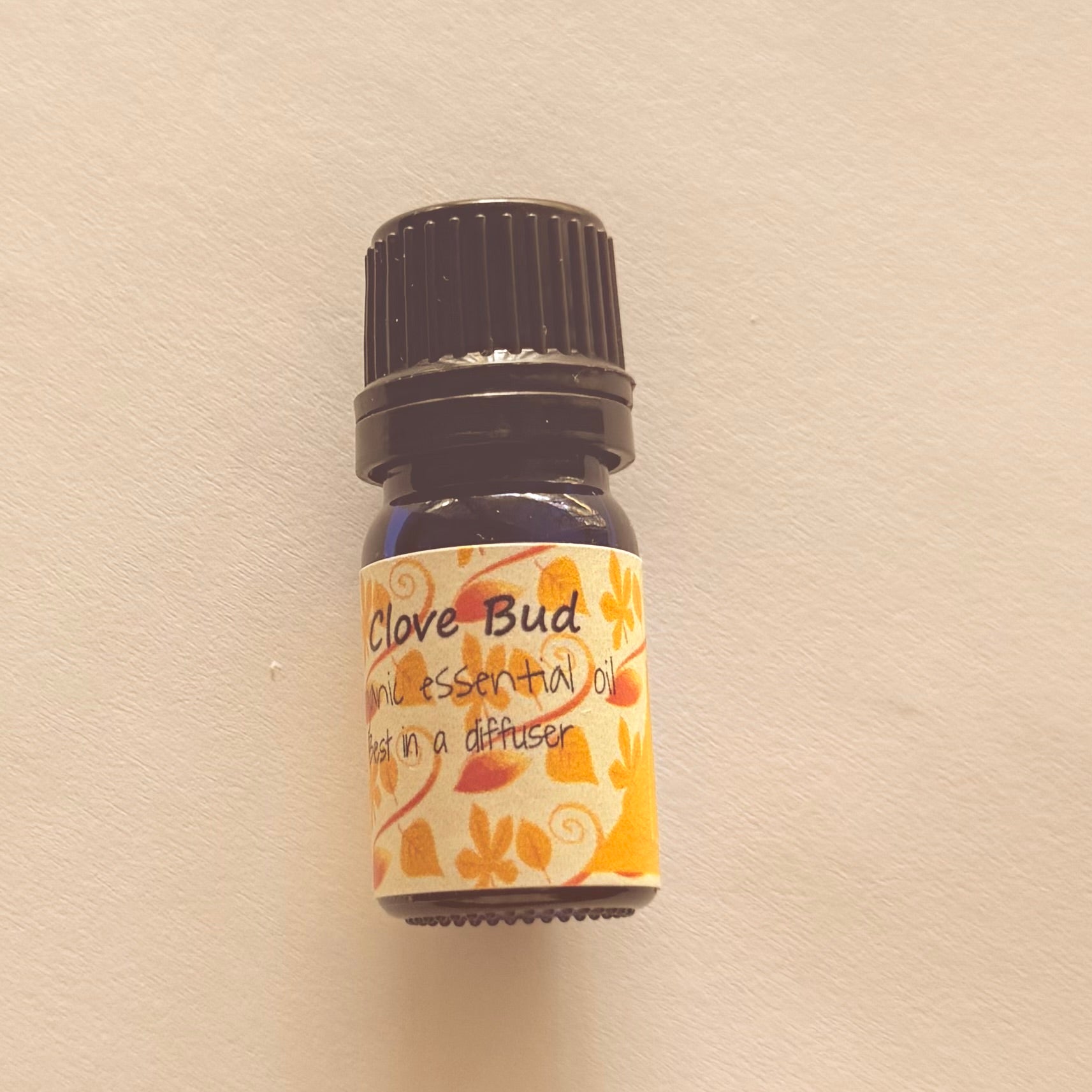 Small bottle of clove bud essential oil with a decorative label on a beige background
