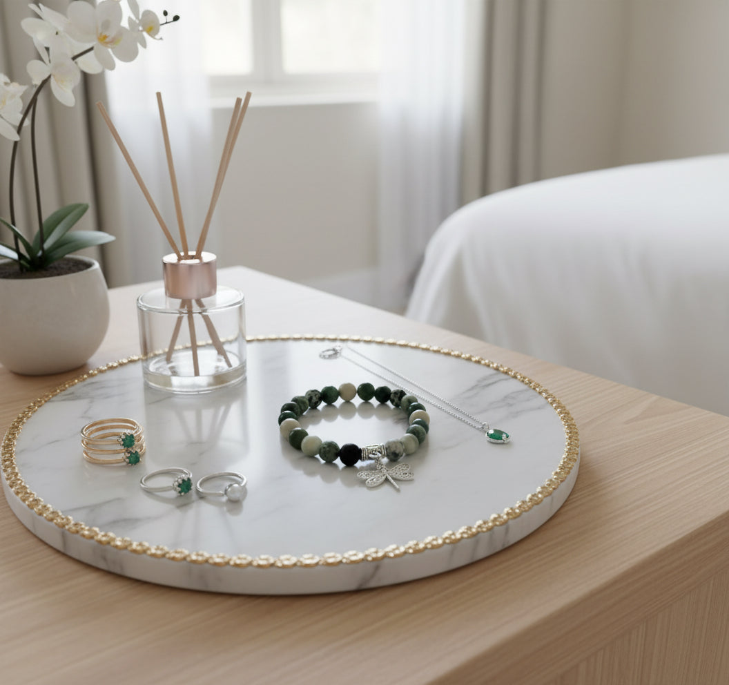 Round marble tray with jewelry on a wooden surface, next to a plant and diffuser.